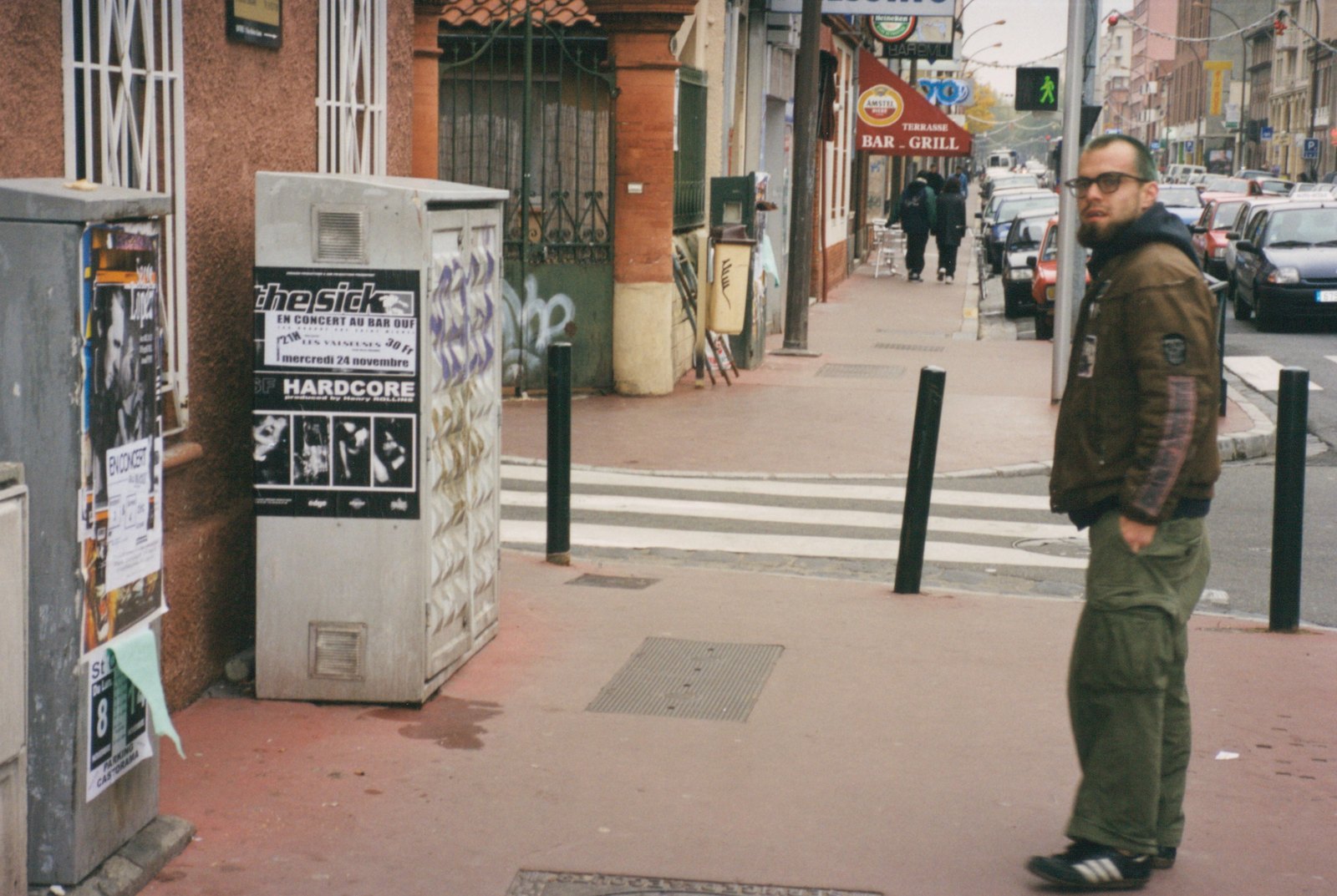 A member of The Sick beside a “The Sick” show poster on a European street, 1999–2000 tour
